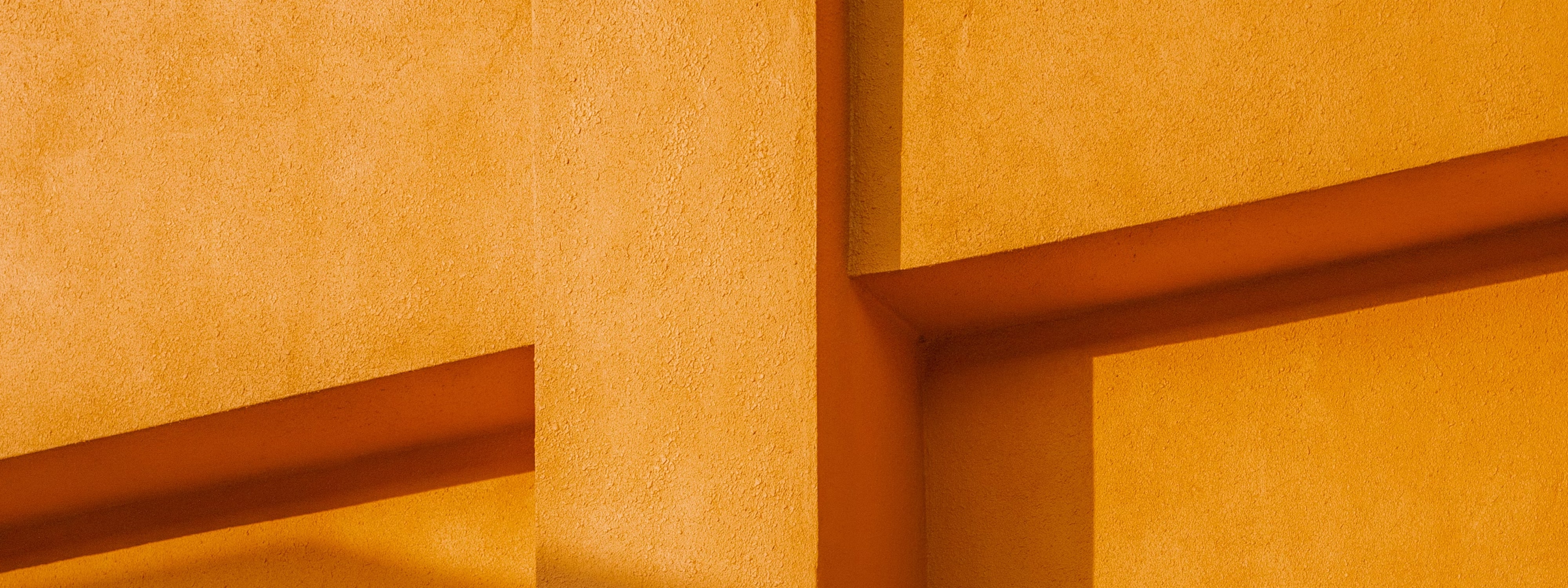 Yellow geometric wall with textured surface and angular architectural shadows