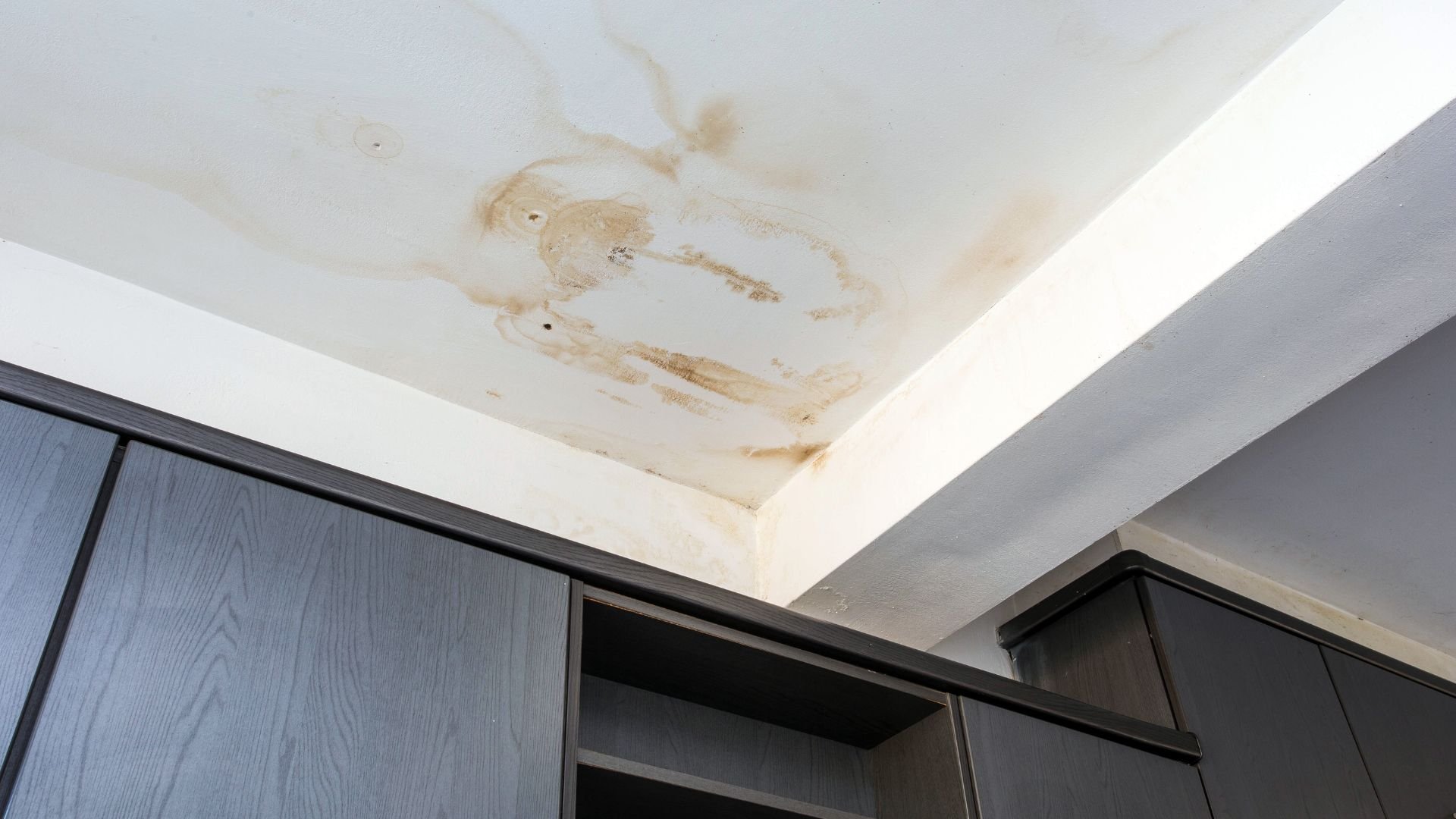 Water stain and damage on white ceiling near dark wooden cabinets