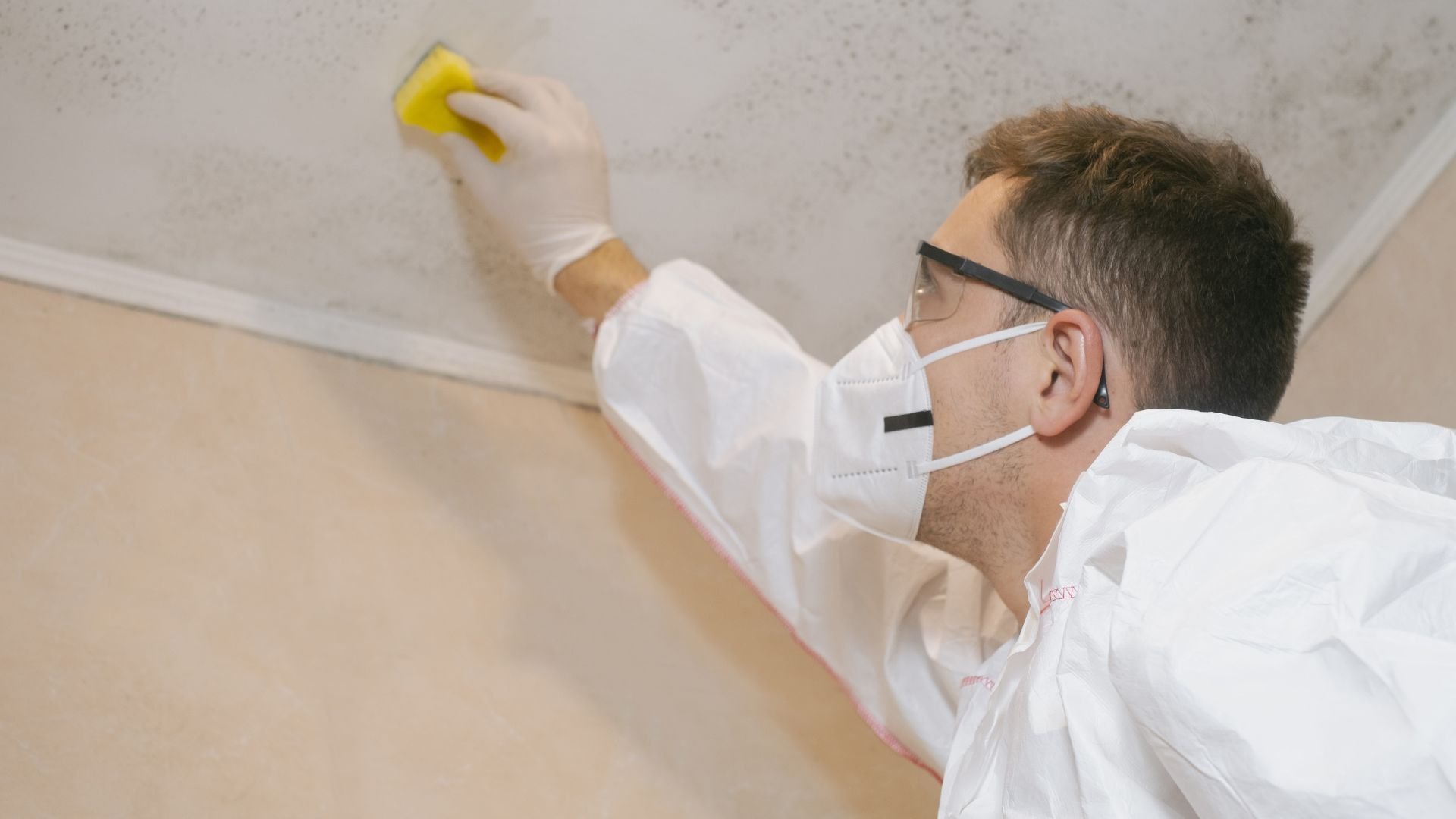 Worker in protective gear cleaning ceiling with yellow sponge