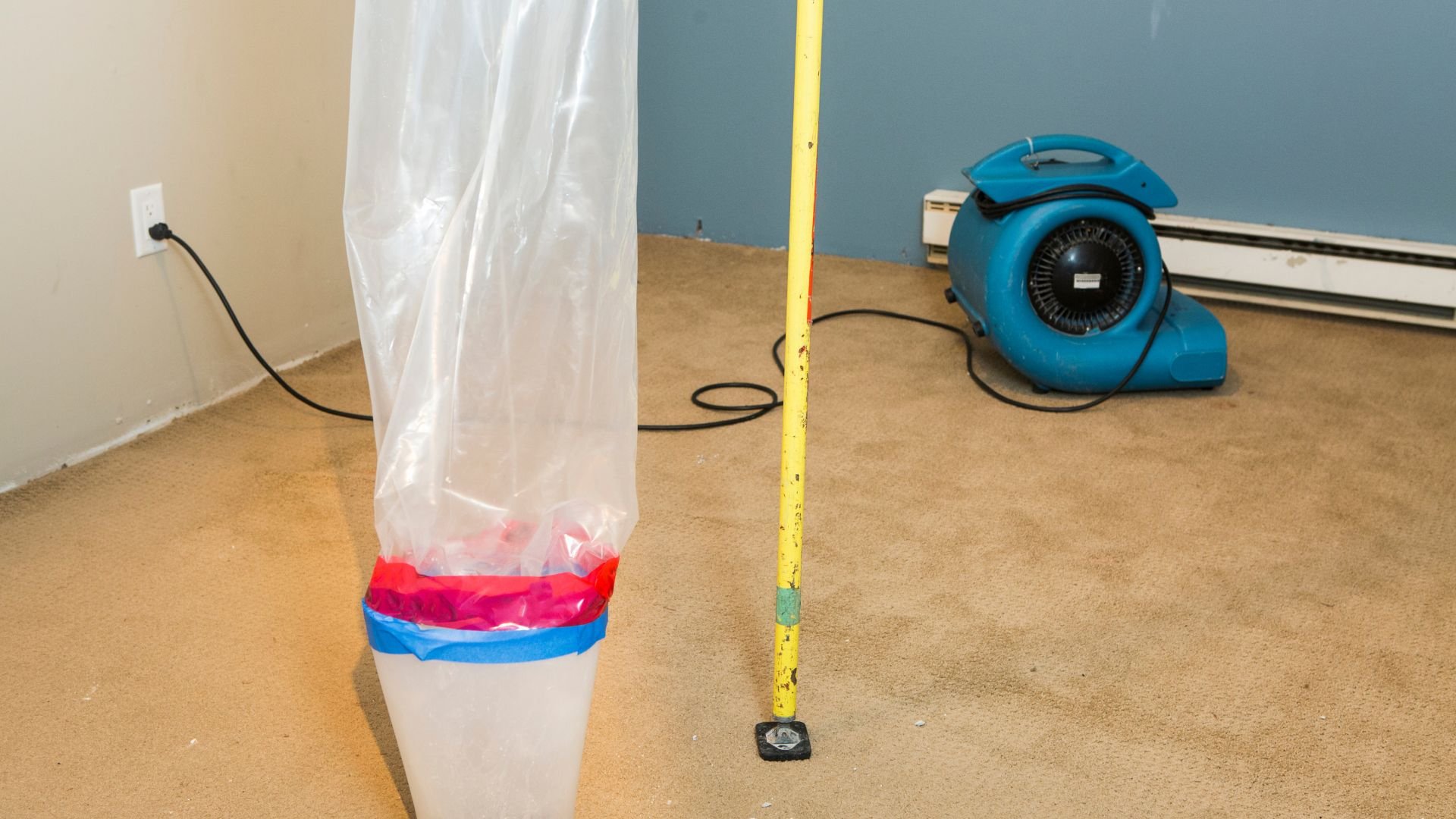 Blue fan and taped plastic sheet on carpet with measuring stick