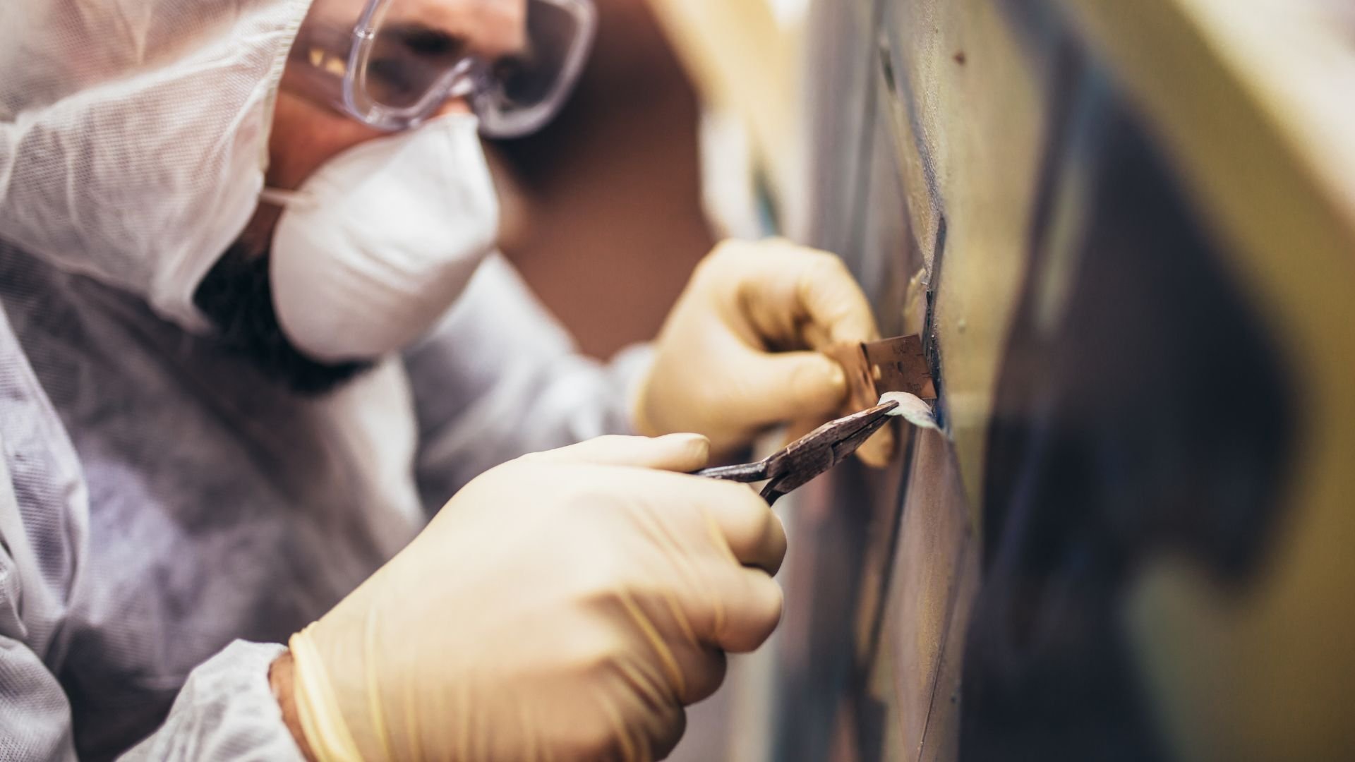 Worker in protective gear using tool to repair or inspect surface